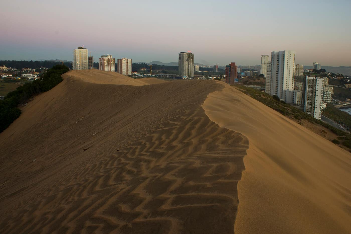 Der Kamm einer großen Sanddüne in Concón mit Hochhäusern am Horizont